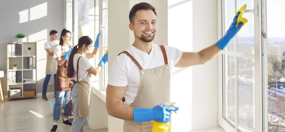 Man from cleaning service using a duster and a spray while cleaning windows in Stock Photos