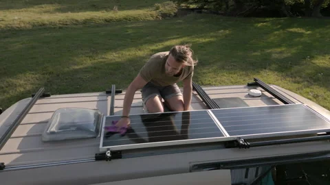Man cleaning a solar panel on top of the roof of his camper van Video stock 225679682