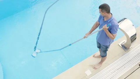 Man cleaning swimming pool with vacuum tube cleaner early in the morning. Stock Footage 112267995