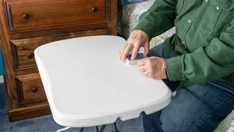 Man Cleaning a Table in a Bedroom While Sitting on a Chair 写真素材