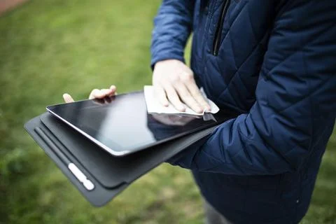 Man cleaning a tablet touchscreen with a tissue in a park Stock Photos
