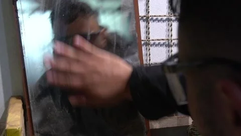 Man cleaning a very old mirror on his workshop. The cluttered space is Stock Footage 235674670