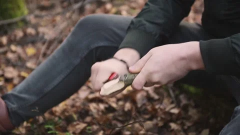 The man cleans and sharpens the stick with his sharp knife. Survival in the wild Stock Footage 142748005
