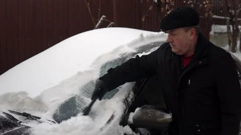 A man cleans a car windshield from snow with a brush. Winter in Russia, the car Stock Footage 145771459