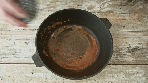 A man cleans a cast iron pan with a metal brush Stock Footage 126398686