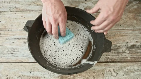 A man cleans a cast iron pan with a sponge and soap Stock Footage 126400382