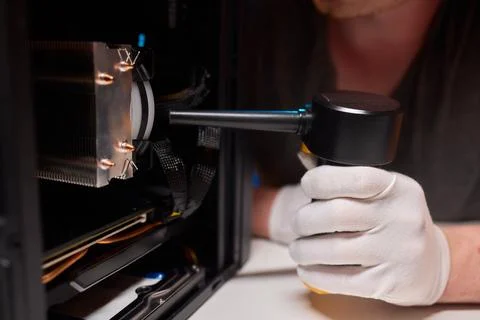 A man cleans a computer case with a vacuum in a bright room, stressing workspace Stock Photos