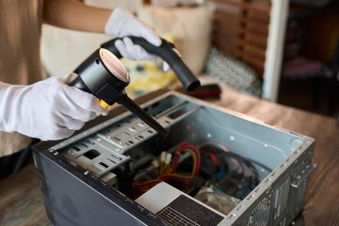 A man cleans a computer case with a vacuum in a bright room, stressing workspace Stock Photos