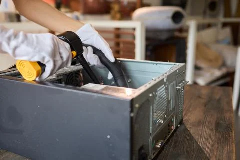 A man cleans a computer case with a vacuum in a bright room, stressing workspace Stock Photos