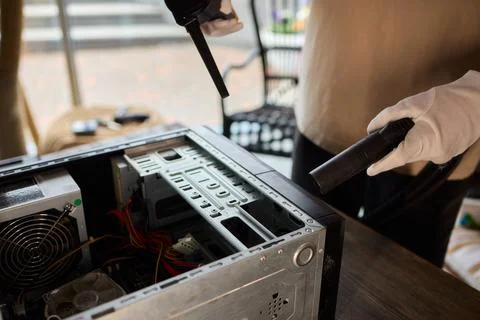 A man cleans a computer case with a vacuum in a bright room, stressing workspace Stock Photos