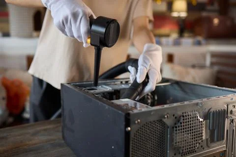 A man cleans a computer case with a vacuum in a bright room, stressing workspace Stock Photos