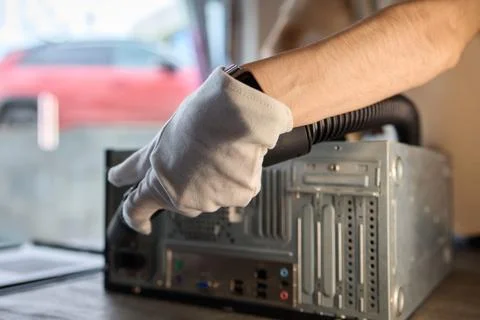 A man cleans a computer case with a vacuum in a bright room, stressing workspace Stock Photos