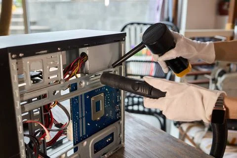 A man cleans a computer case with a vacuum in a bright room, stressing workspace Stock Photos