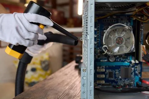 A man cleans a computer case with a vacuum in a bright room, stressing workspace Stock Photos
