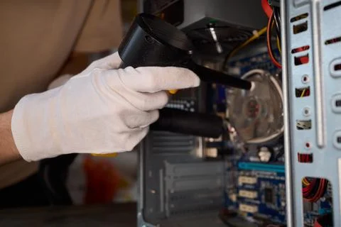A man cleans a computer case with a vacuum in a bright room, stressing workspace Stock Photos
