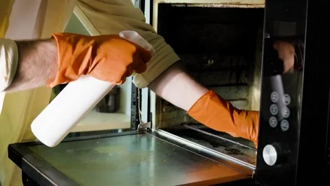 Man cleans a dirty kitchen oven using spray cleaner detergent and a sponge. He w Vídeo Stock 346723235