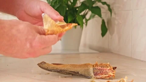 A man cleans dried fish in the kitchen. The guy separates the meat and bones of Stock Footage 244637814