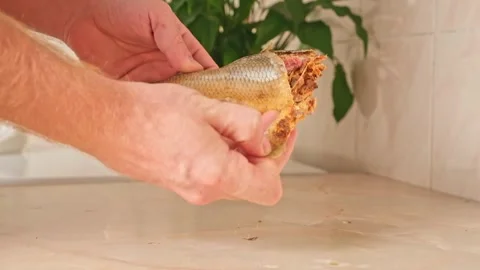 A man cleans dried fish in the kitchen. The guy separates the meat and bones of Stock Footage 244803753