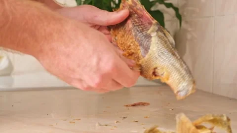 A man cleans dried fish in the kitchen. The guy separates the meat and bones of Stock Footage 245208937