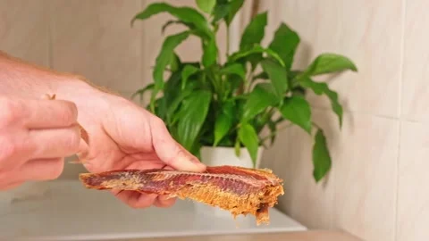 A man cleans dried fish in the kitchen. The guy separates the meat and bones of Stock Footage 246641349