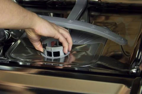 Man cleans the filter in the dishwasher. Maintenance of home appliances. Stock Photos