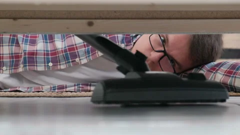 A man cleans the floor with a vacuum cleaner under a bed or sofa, closeup Video stock 127780265