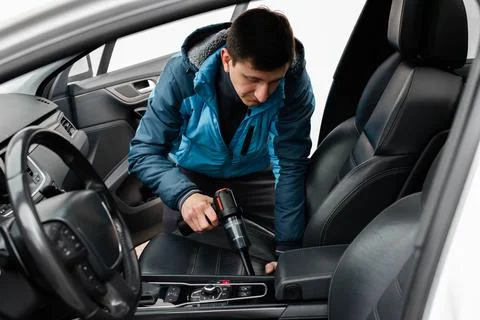 A man cleans the front leather seats inside a modern car interior 스톡 사진