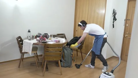 A man cleans his apartment in general shot, vacuums Stock Footage 199128288