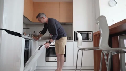 The man cleans the kitchen, takes out clean dishes from the dishwasher. Stock Footage 160887628
