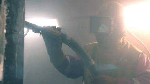Man cleans metal surface by sandblaster gun in a metal construction factory Stock Footage 95735498
