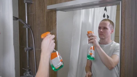 A man cleans the mirror in the bathroom. A young man cleans the bathroom mirror Stock Footage 95962883