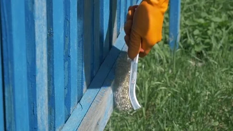 Man cleans old blue paint from fence with metal brush Stock-Footage 114576800