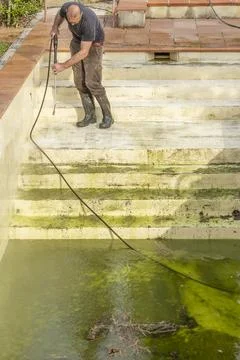 A man cleans a pool completely covered in dirt and algae Fotos de archivo
