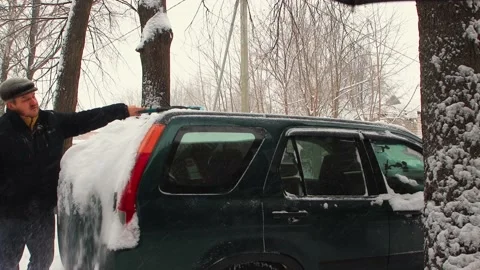 A man cleans the rear window of the car from snow with a brush, it is snowing. Stock Footage 224680161