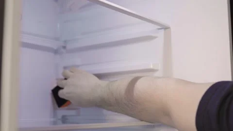 Man cleans up  a refrigerator shelf. Kitchen chores. Man cleaning fridge with sp Stock Footage 305341742