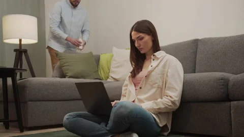 The man cleans the room while the girl works at the computer. Stock Footage 154567077