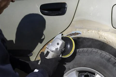 A man cleans up rust on a car with an angle grinder Stock Photos