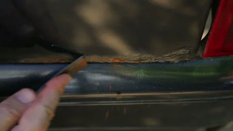 A man cleans rust on a car body with a scraper Видео 119923530