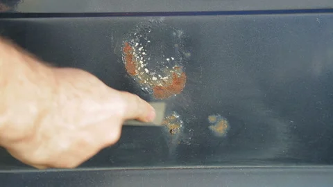 A man cleans rust on a car with a scraper Stock Footage 113829330