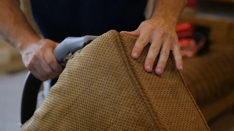 Man cleans the side of a couch cushion with a hand held wet vacuum Stock-Footage 85869625
