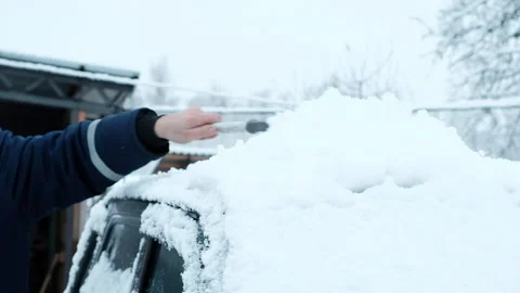 A man cleans snow from a car with a brush. Stock Footage 168057449