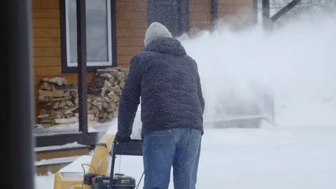 A man cleans snow with a snow blower near his house. 動画素材 122336396