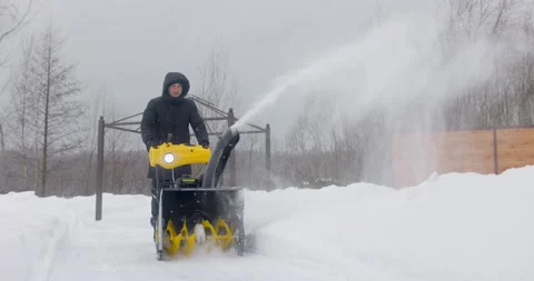 A man cleans the snow with a snowblower in yard at snowfall in slow motion Stock Footage 169659547