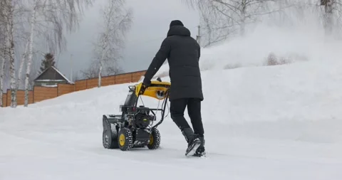 A man cleans the snow with a snowblower in yard at snowfall in slow motion Stock Footage 169659567