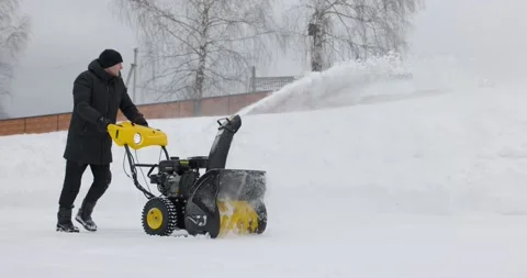 A man cleans the snow with a snowblower in yard at snowfall in slow motion Stock Footage 169659599