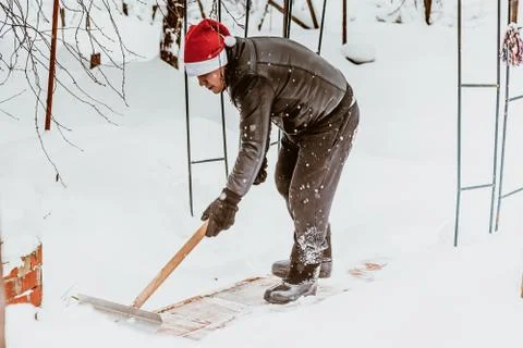A man cleans steps from snow. In a red hat of Santa Claus and a leather black Stock Photos