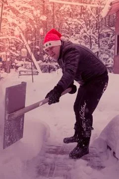 A man cleans steps from snow. In a red hat of Santa Claus and a leather black Stock Photos