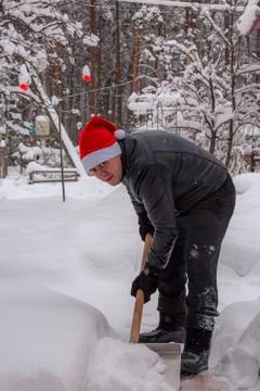 A man cleans steps from snow. In a red hat of Santa Claus and a leather black Stock Photos