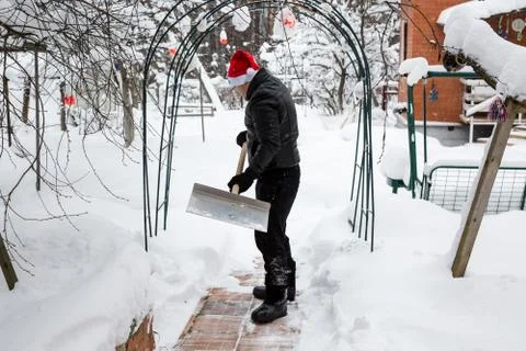 A man cleans steps from snow. In a red hat of Santa Claus and a leather black Stock Photos