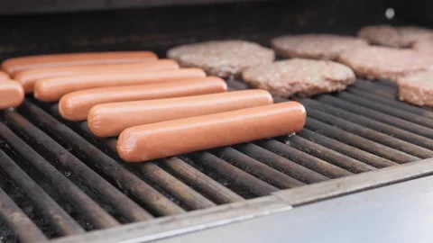 Man cleans surface of grill while hotdogs and burgers cook Video stock 121404557